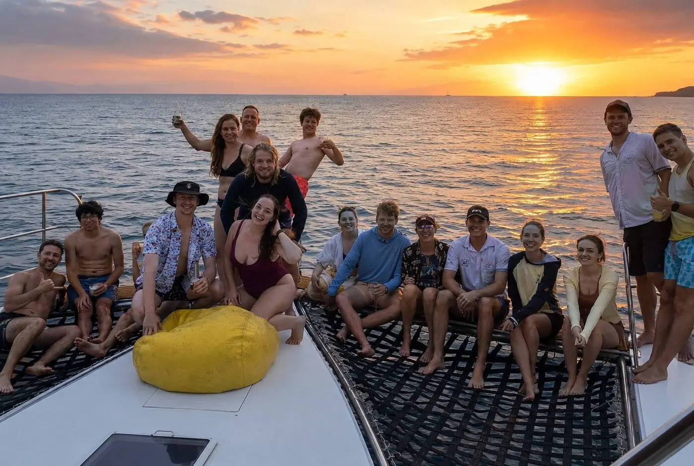 A large group gathers on the catamaran's bow netting as the sun sets over Banderas Bay