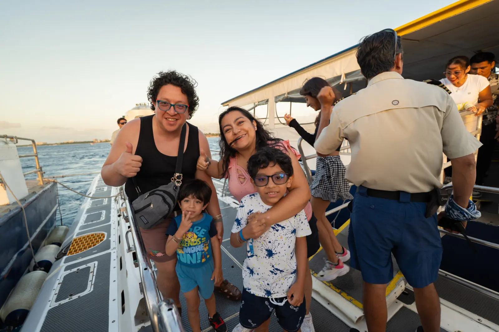 Family with two kids giving thumbs-up on deck beside a uniformed crew member in Cozumel