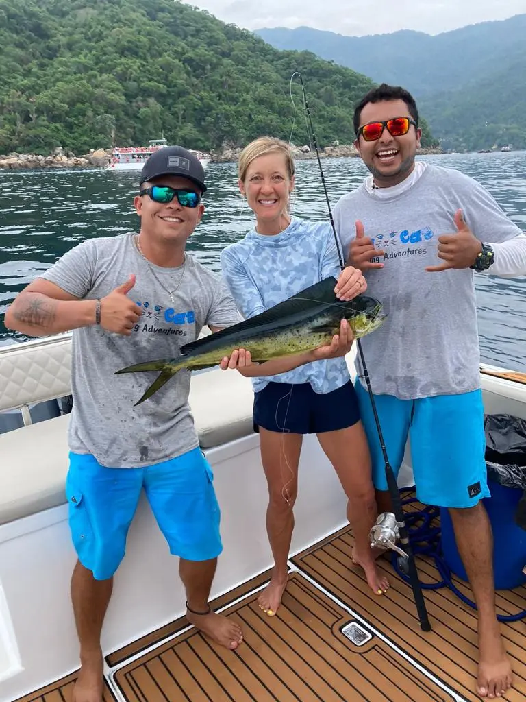 Two men and a woman giving a thumbs-up with a freshly caught mahi-mahi on the boat's teak deck