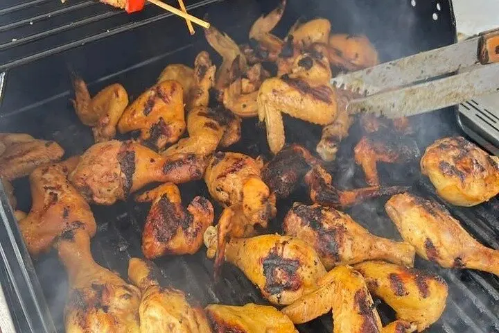 Chicken drumsticks and thighs browning on a hot barbecue grill with tongs