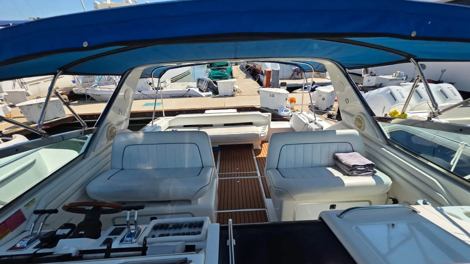 Helm controls and white captain's chairs looking aft across the yacht's teak cockpit to the marina