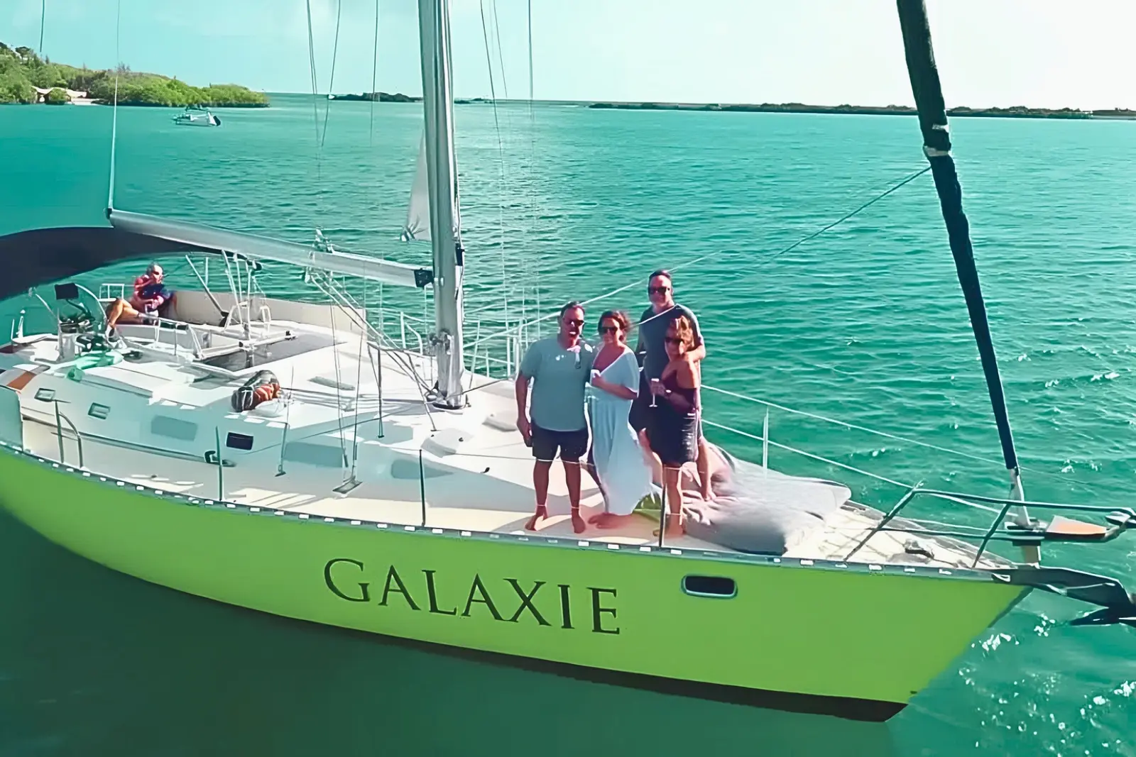 Lime-green sailing yacht at anchor in turquoise Curaçao water with four guests posing on deck