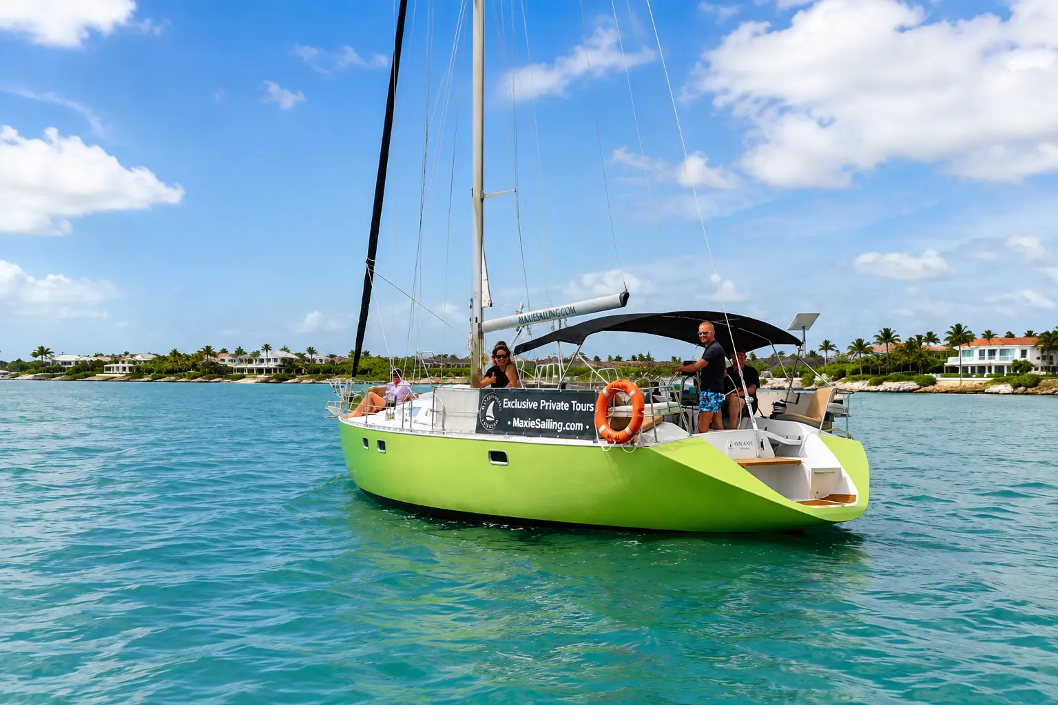 Lime-green sailing yacht with guests aboard on calm water off a palm-lined Curaçao shore