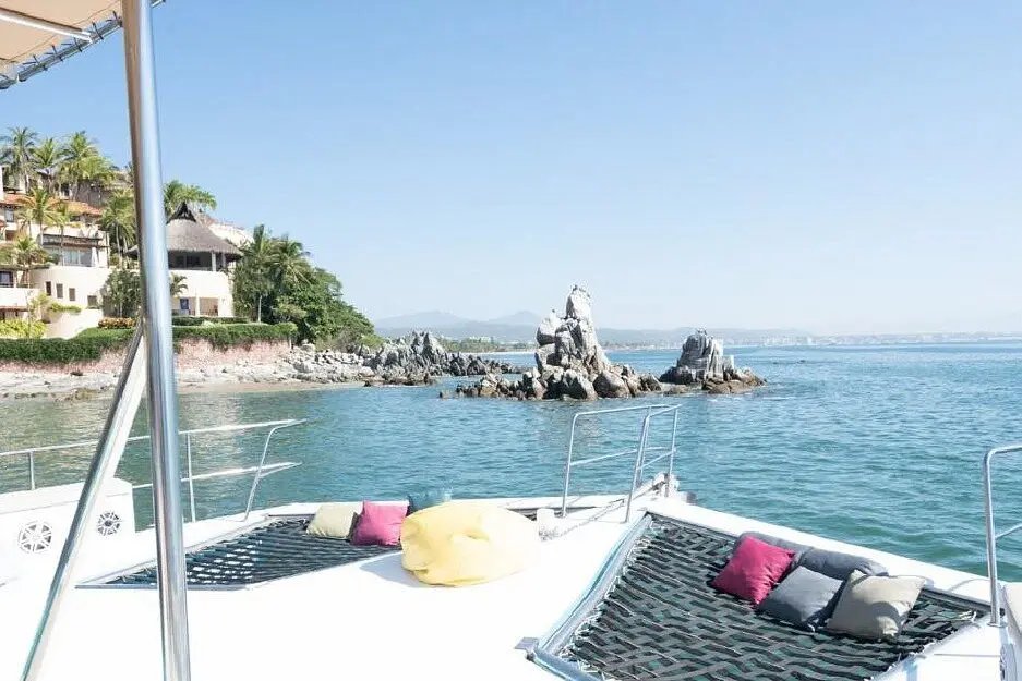 Catamaran bow nets with cushions and a bean bag facing rocky islets and hillside villas on Banderas Bay