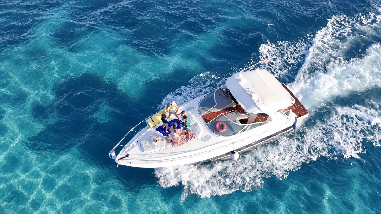 Aerial view of an express cruiser speeding over turquoise water off Cancún, guests lounging on the bow