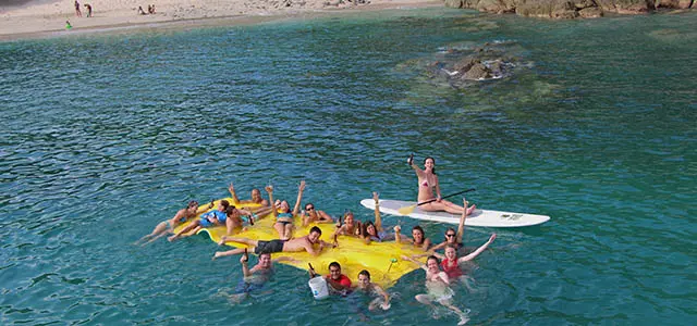 Aerial view of guests piled on a yellow floating mat beside a paddleboard near a Puerto Vallarta beach