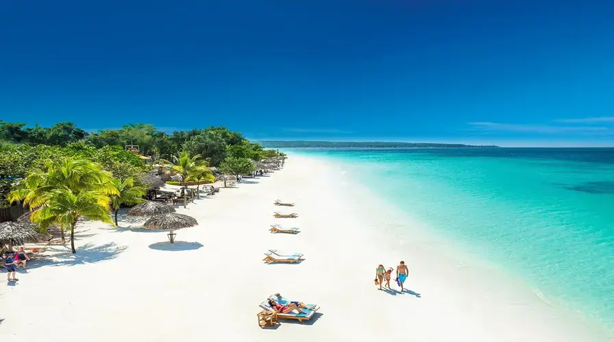 Aerial view of a white sand beach in Negril with palms, thatched umbrellas and sun loungers by turquoise water