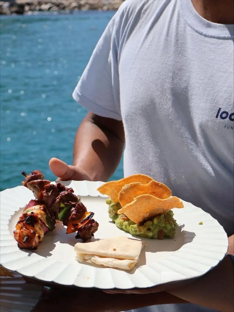 A crew member holds a plate of grilled skewers, guacamole, tortilla chips and a folded tortilla