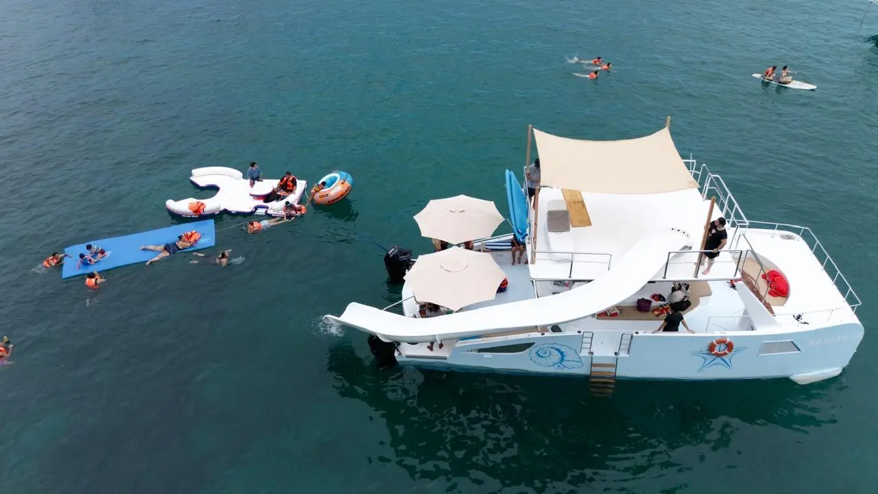 Overhead view of the party catamaran's slide and shade umbrellas as guests float on a mat and inflatables