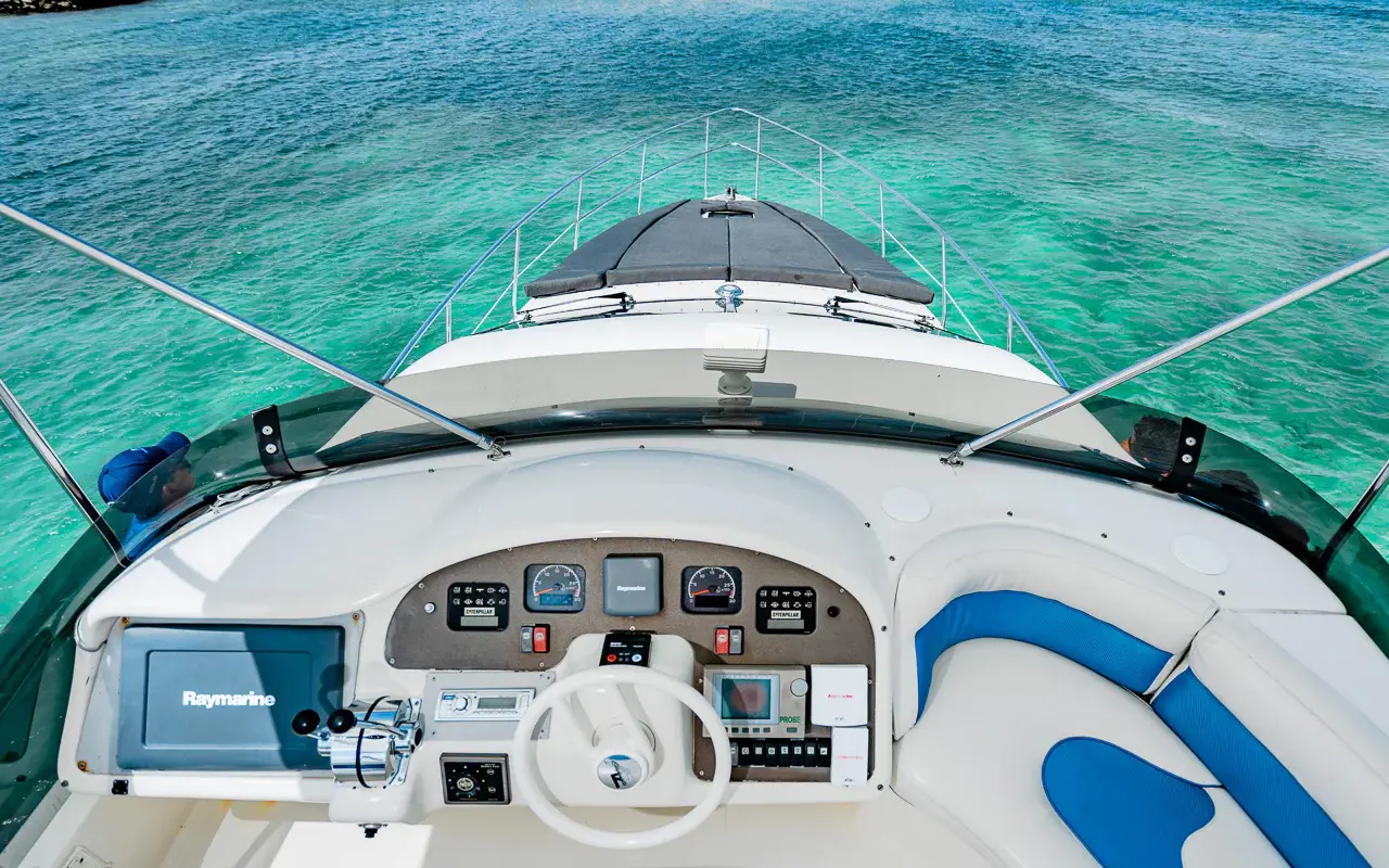 Yacht flybridge helm with wheel, gauges and blue-and-white seating overlooking the bow and turquoise water