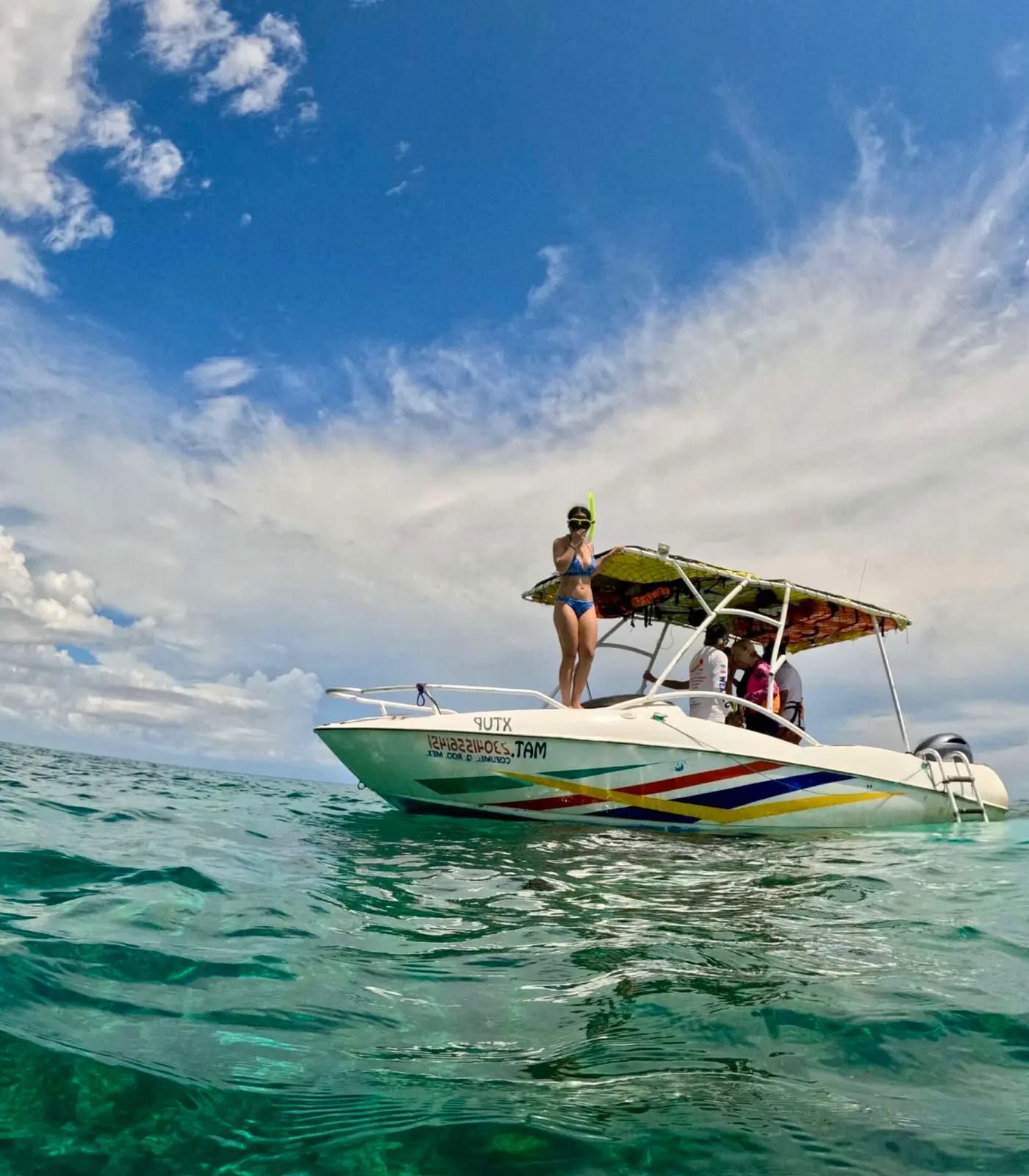 Speedboat with a striped hull anchored in calm turquoise water off Cozumel as a guest stands on the bow