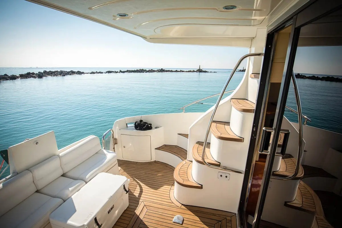 Aft deck of the motor yacht with white bench seating and teak steps to the flybridge, calm water beyond