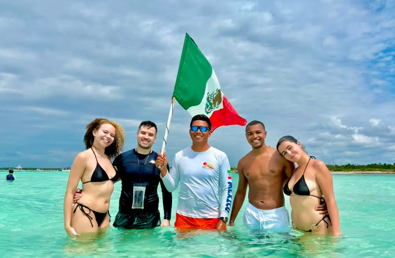 Guide holding a Mexican flag with four guests standing in shallow turquoise water off Cozumel