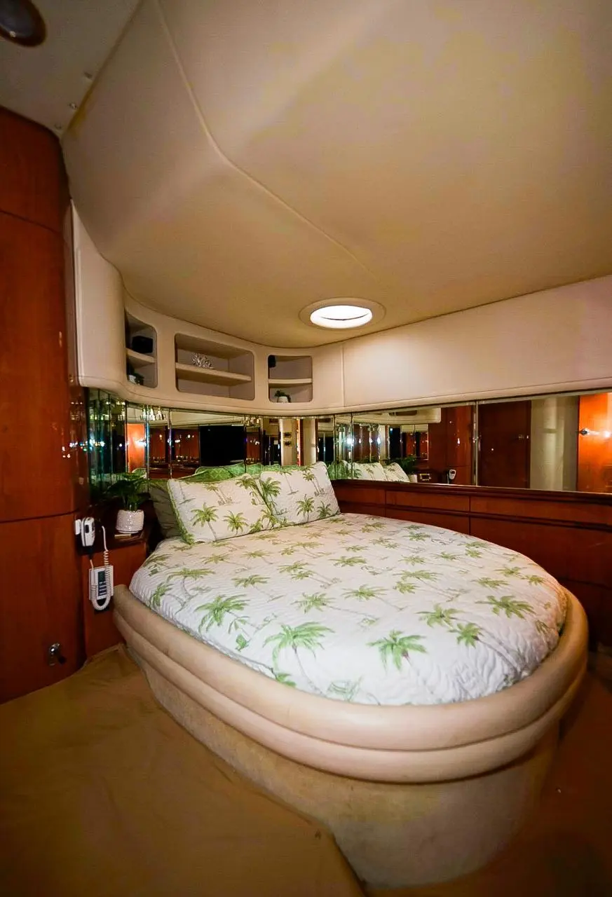 Yacht cabin with an island double bed in palm-leaf print linens and glossy cherry wood paneling