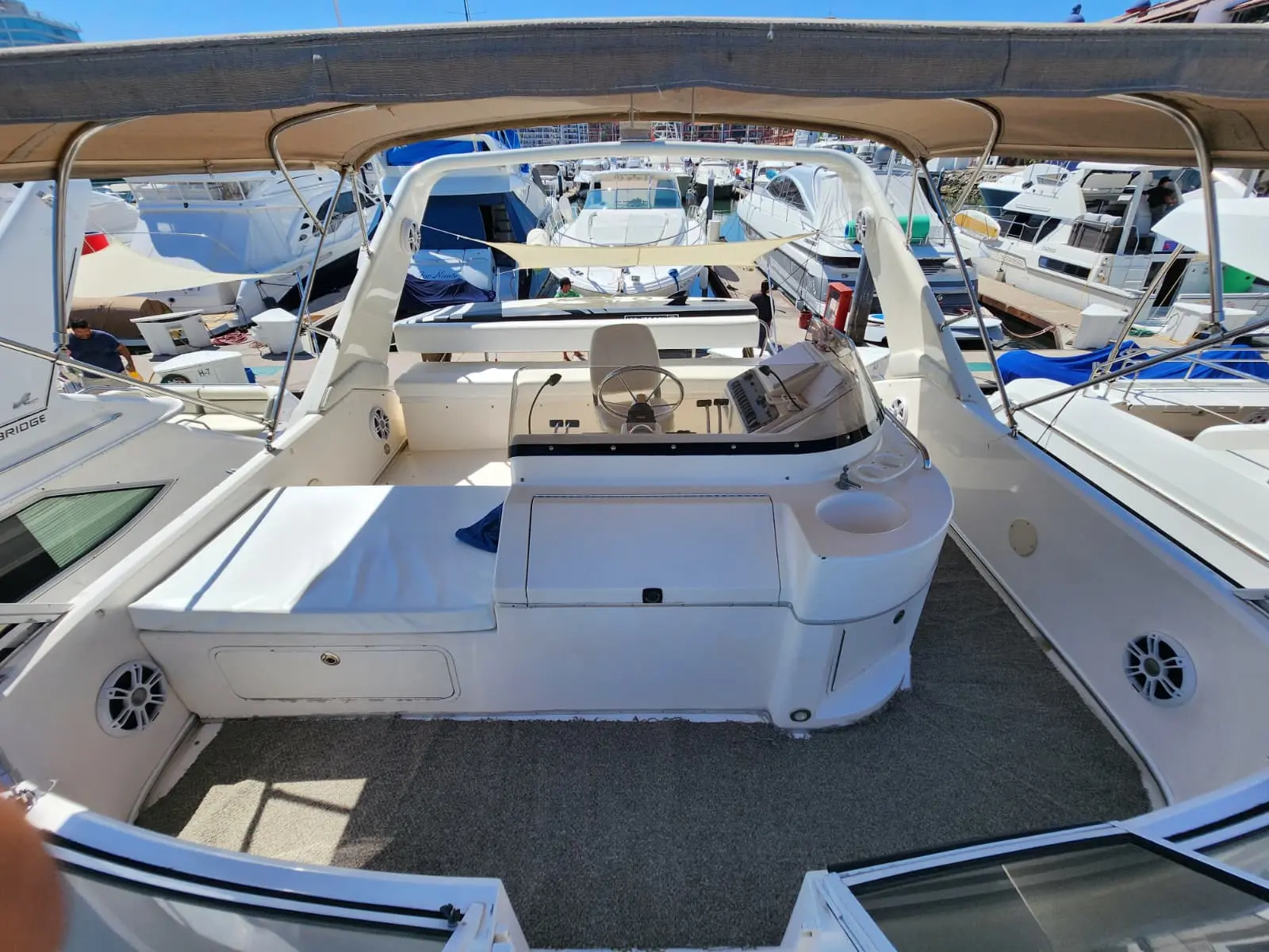 Upper helm deck of the yacht with a captain's seat and console under a tan bimini, marina boats all around