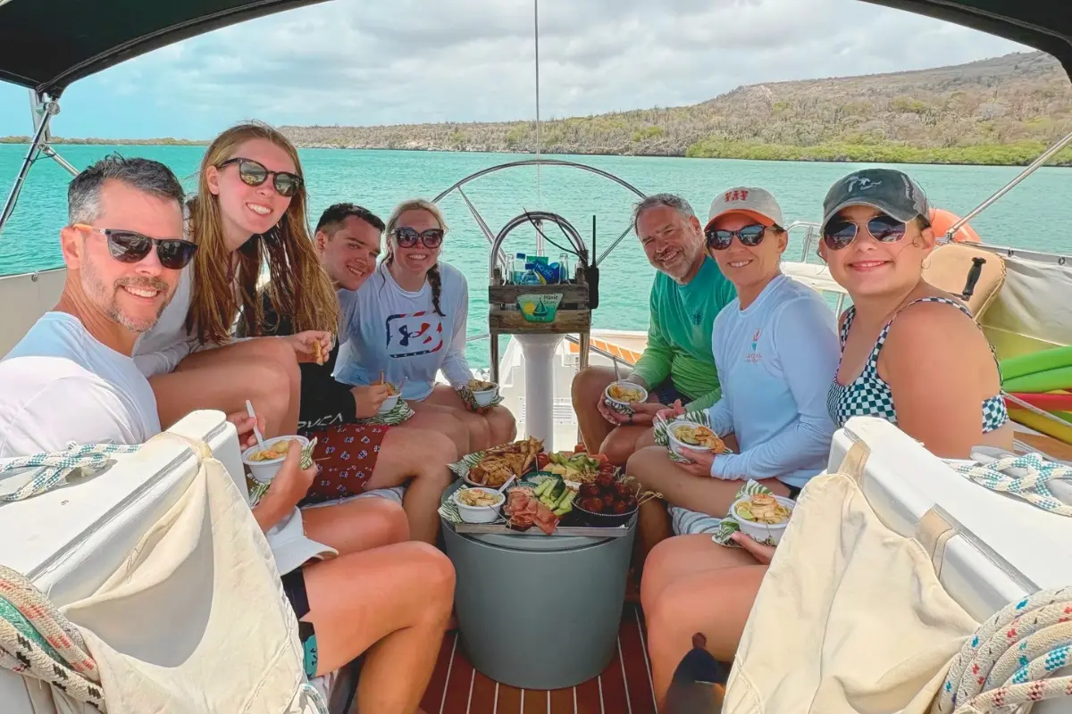 Seven guests sharing snack bowls around the cockpit table of a sailing yacht in Curaçao