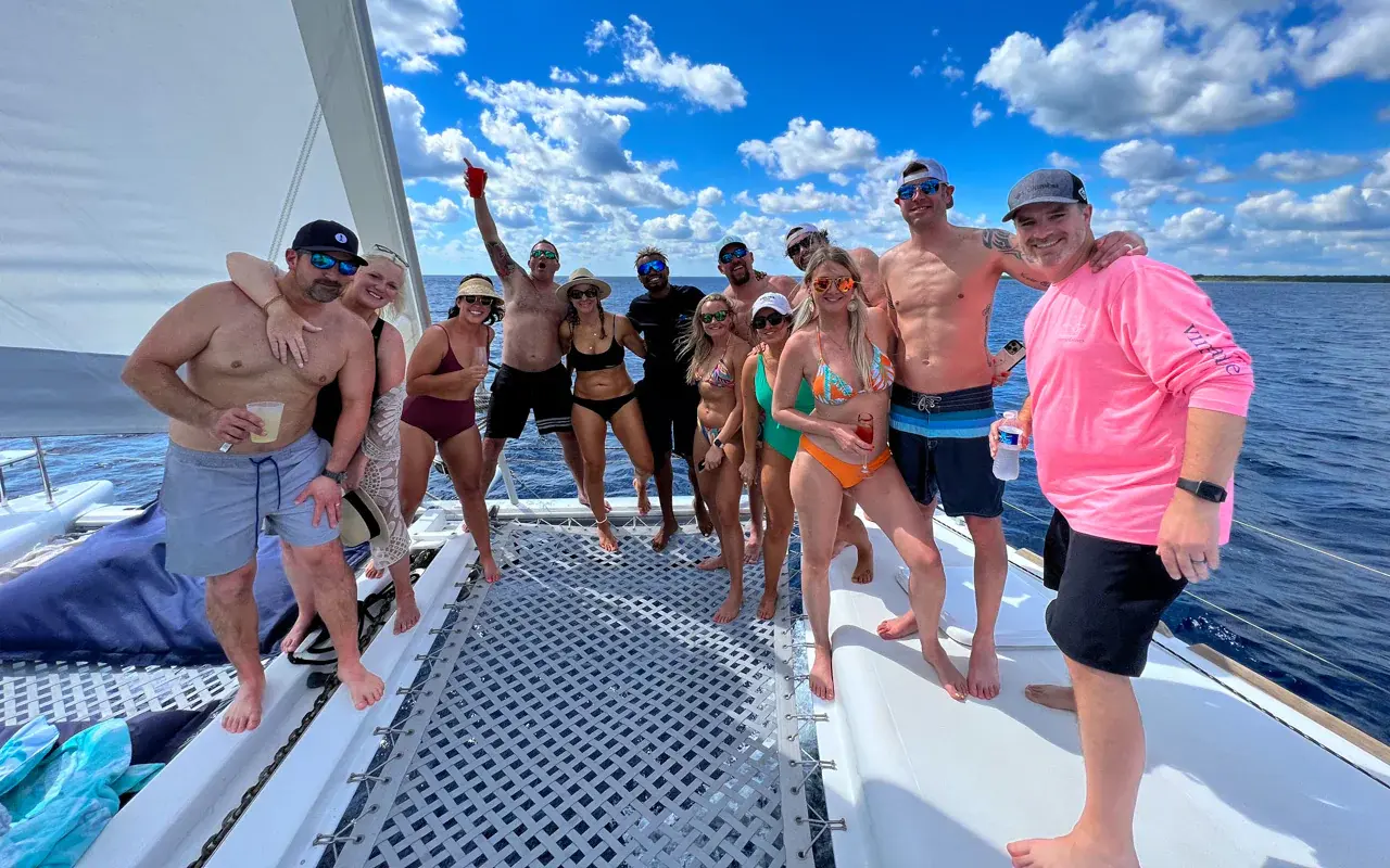 Large group of guests posing on the catamaran's foredeck and trampoline under blue sky