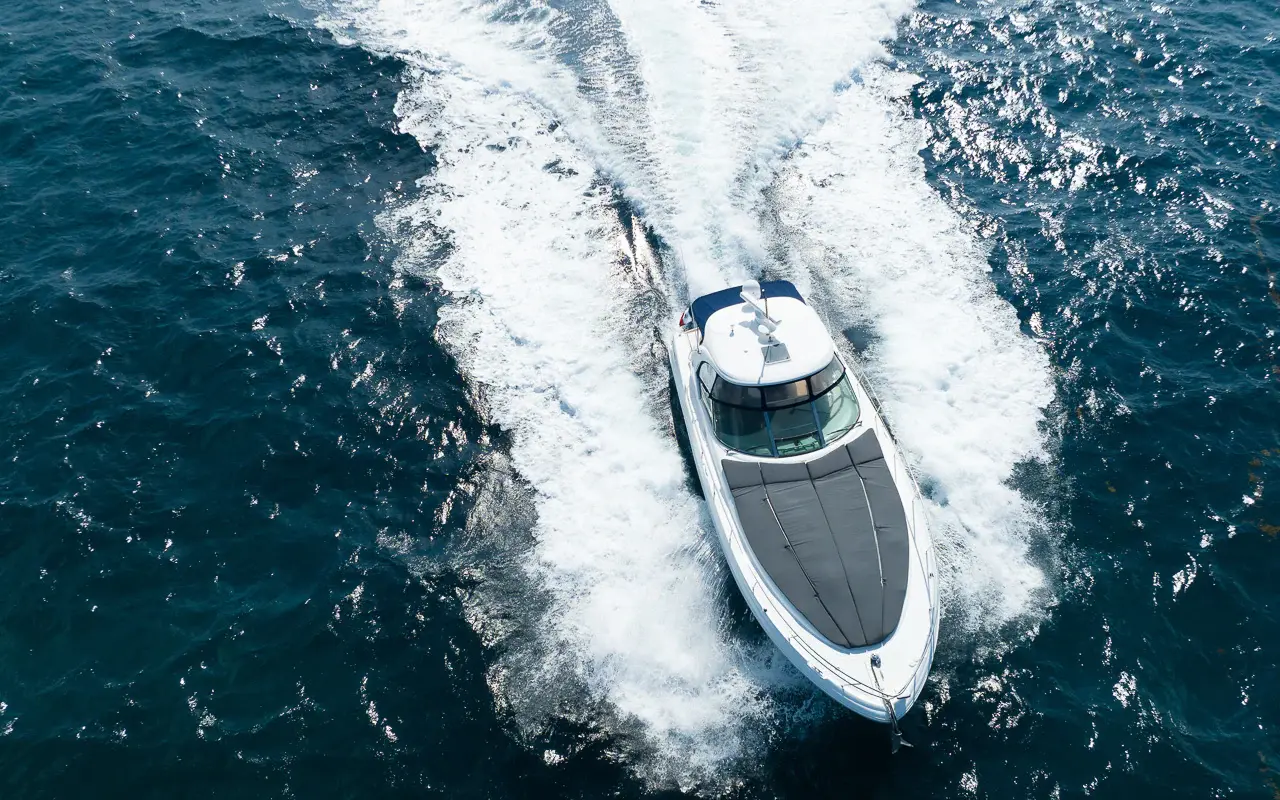 Overhead drone view of the motor yacht cutting a wide white wake through dark blue Riviera Maya water