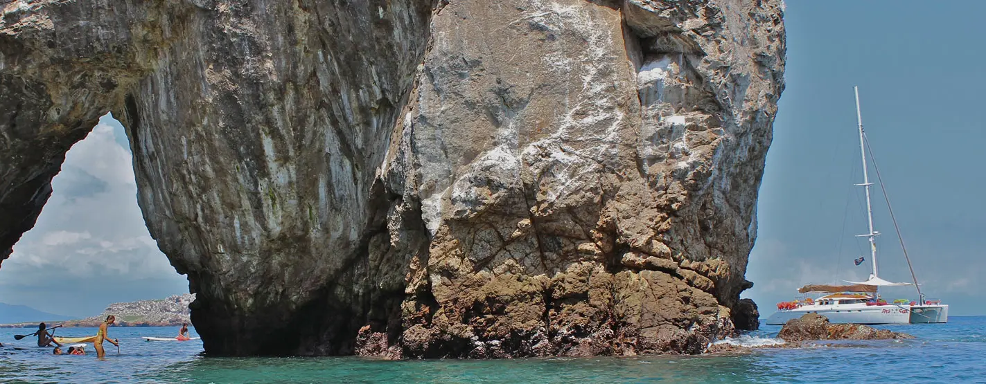 Sailing catamaran anchored near a towering rock arch with snorkelers in the water off Puerto Vallarta