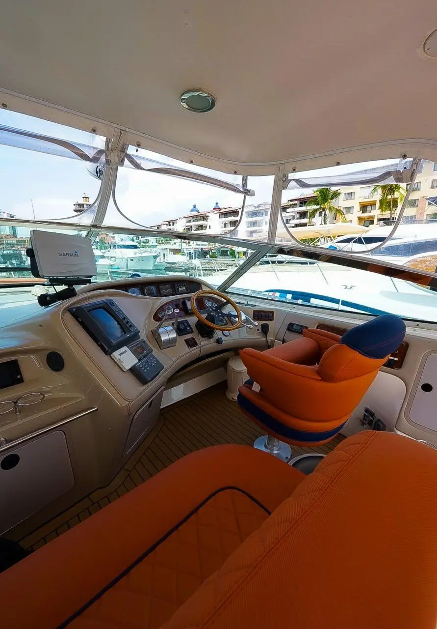 Yacht helm with dashboard screens, steering wheel and orange captain's seat behind the windshield