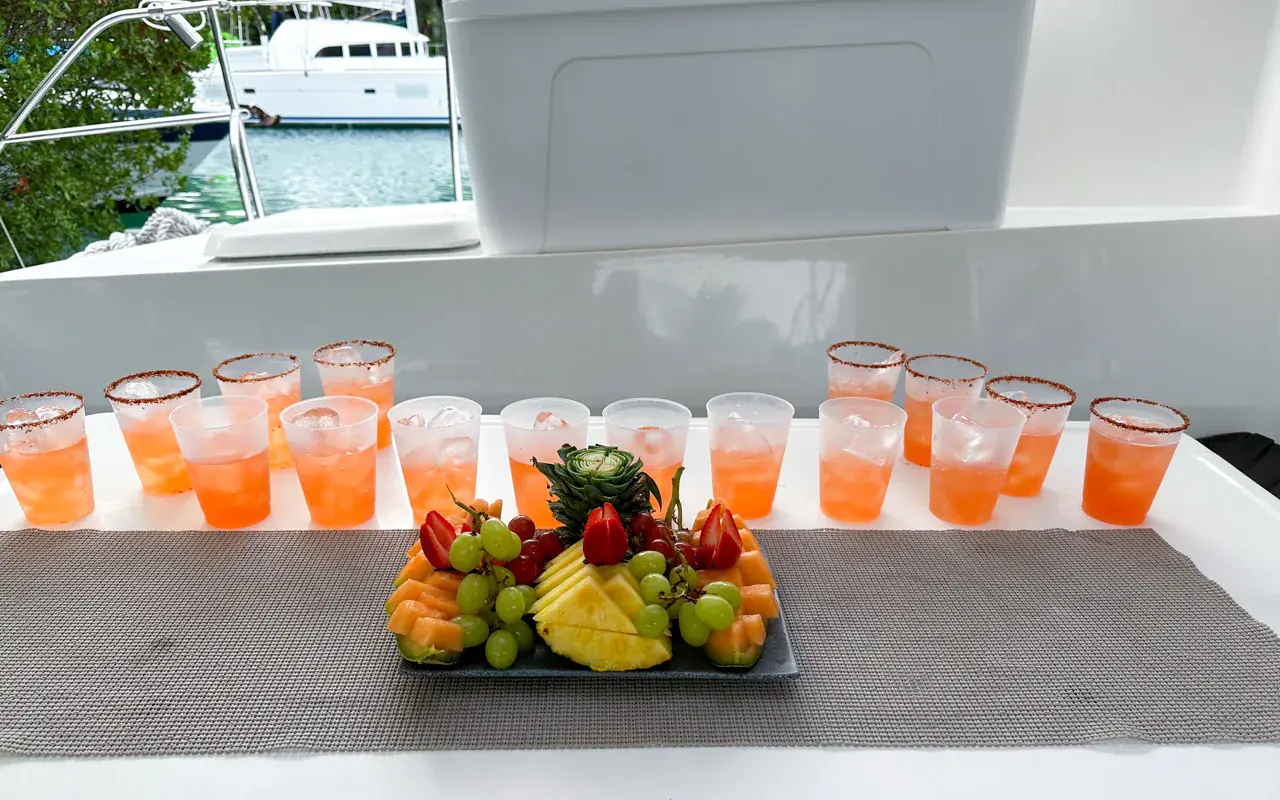 Rows of orange cocktails and a platter of fresh fruit laid out on a counter aboard the yacht