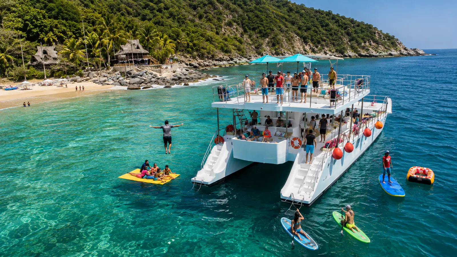 A two-deck catamaran anchored off a jungle beach as guests swim, paddleboard and jump into Banderas Bay