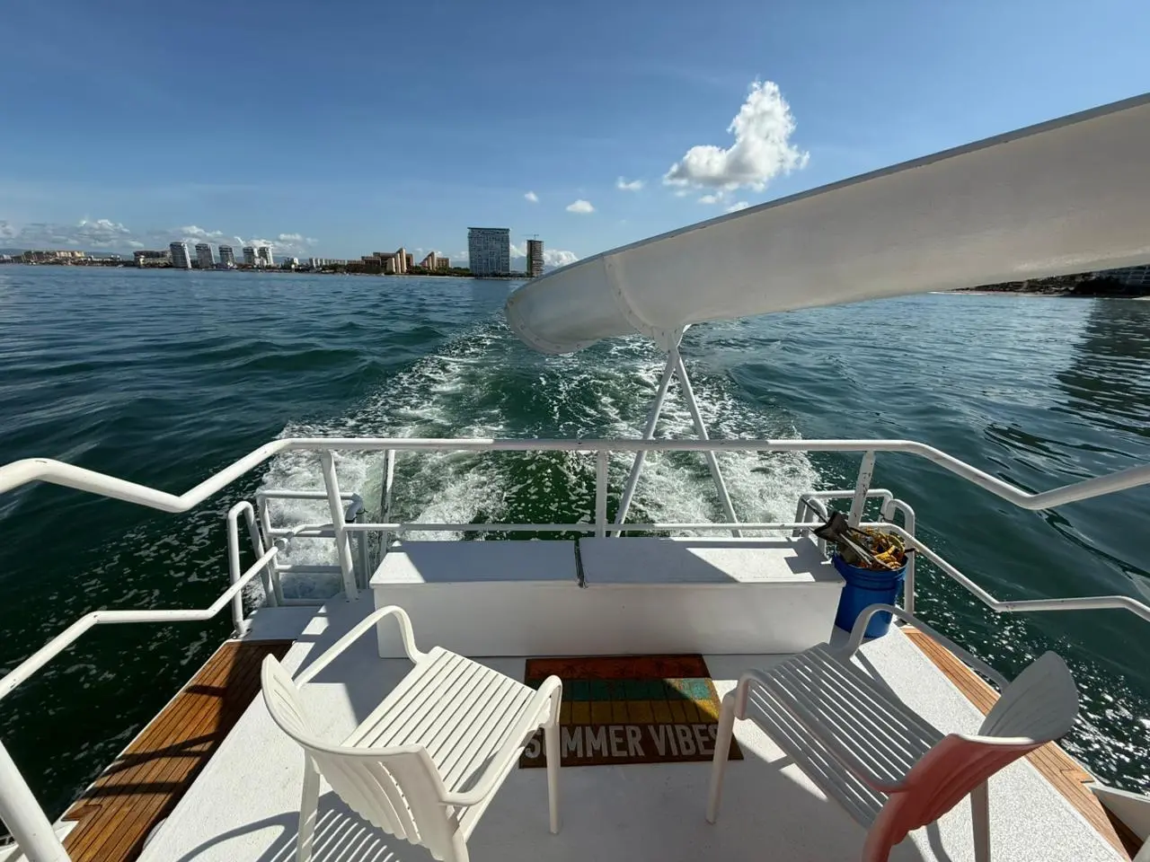 White chairs on the catamaran's stern beneath the water slide, wake trailing toward the Puerto Vallarta shore