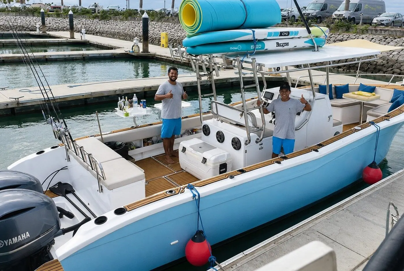 Light blue center console boat docked at the marina with paddleboards on its hardtop and two men aboard