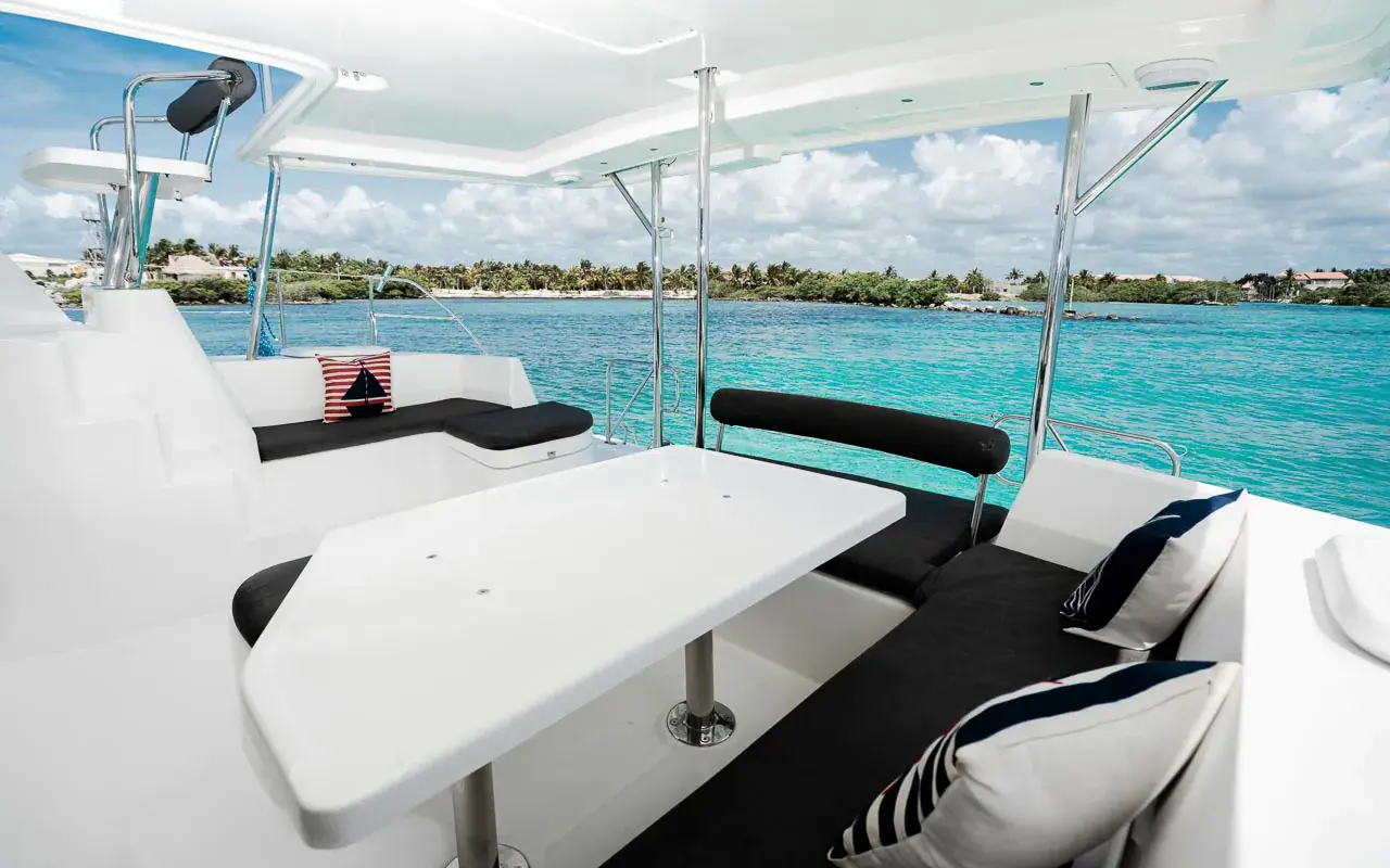 Shaded cockpit with a white table and black-cushioned seating, turquoise water and shoreline beyond