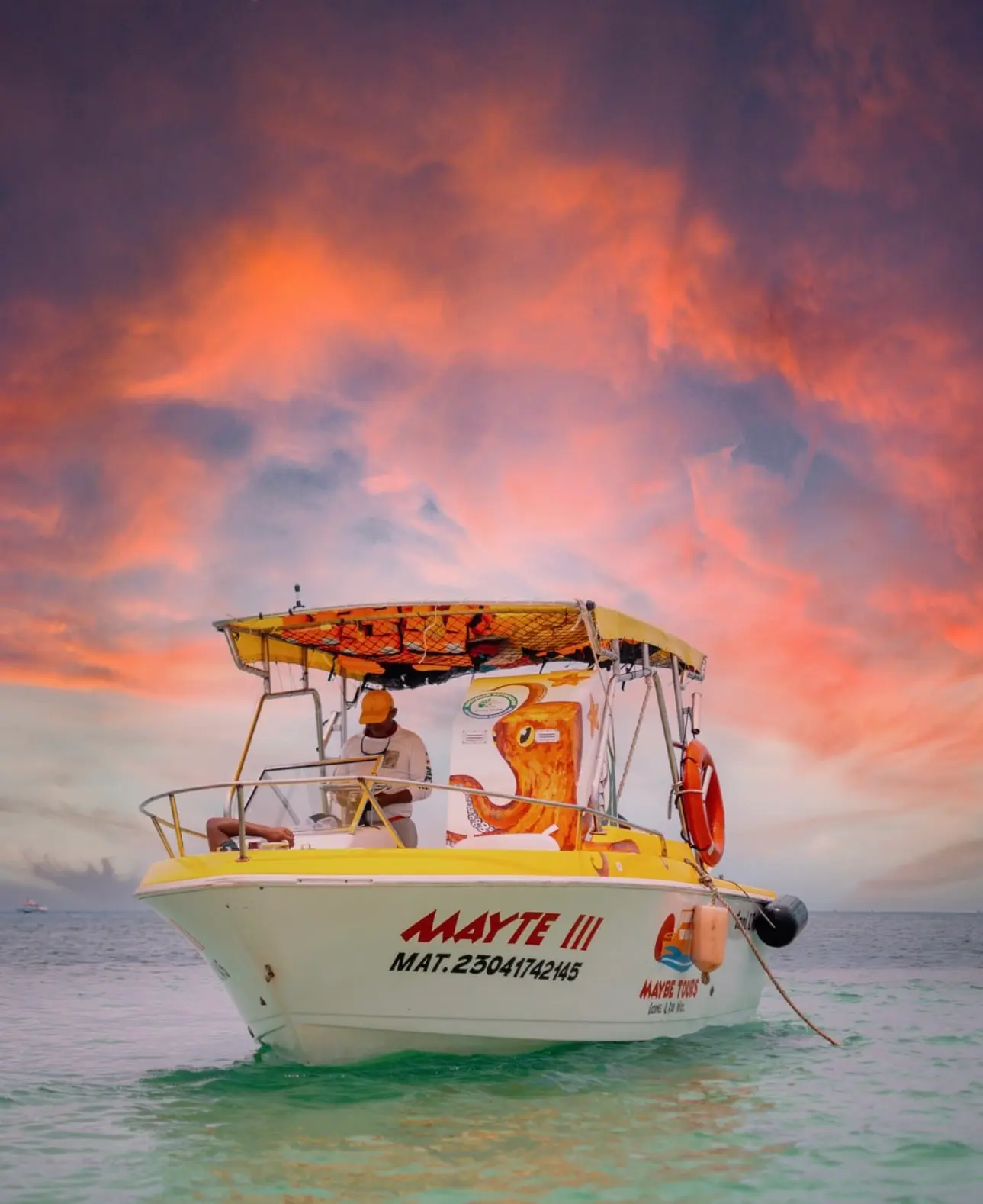 Small speedboat with a yellow canopy floating in turquoise shallows under a fiery pink sky in Cozumel