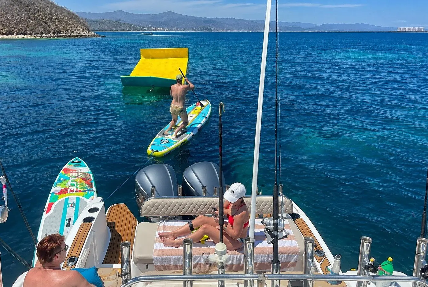 Looking down past the cruiser's twin outboards as a guest paddleboards toward a floating mat in the bay