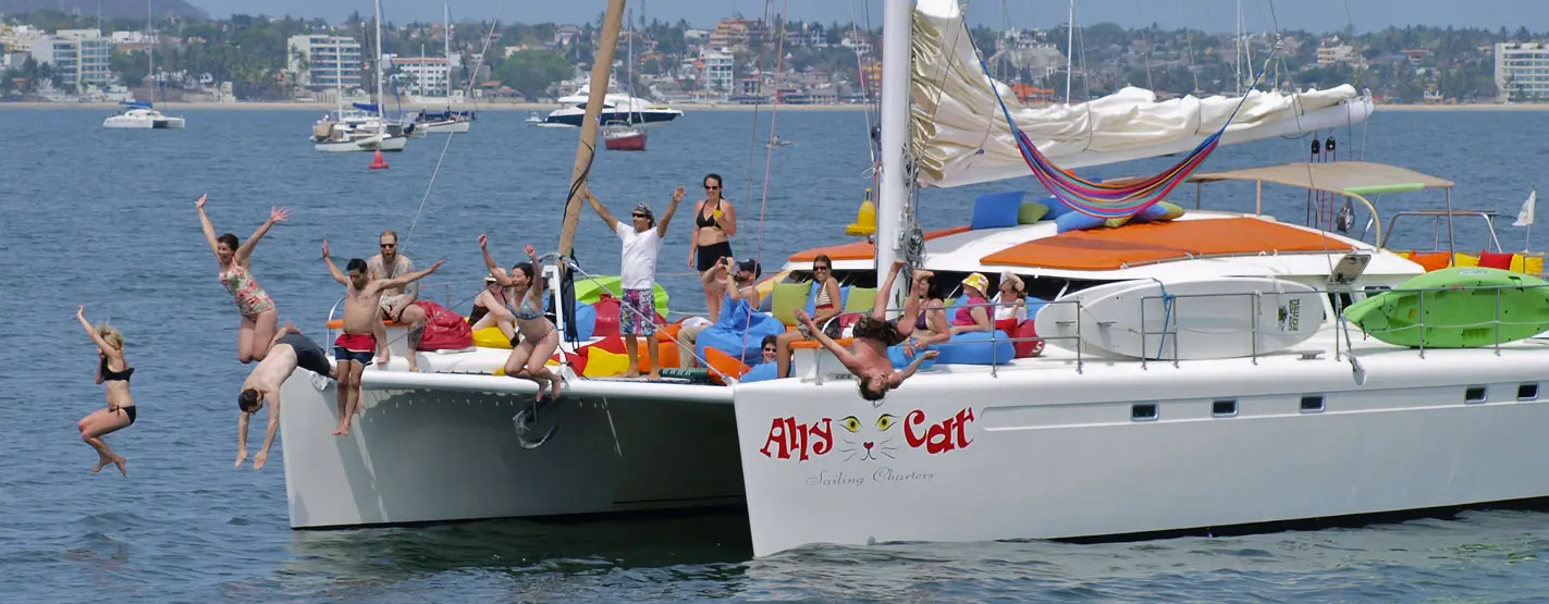 Guests leaping off the sailing catamaran into the bay with the Puerto Vallarta waterfront behind