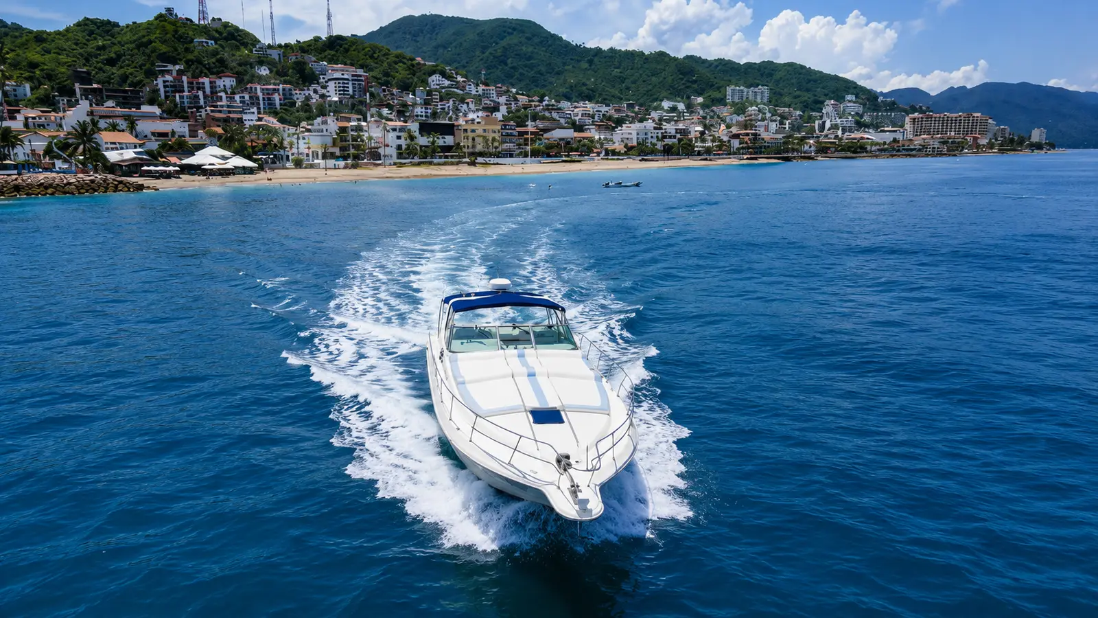 A white motor yacht speeds across the bay with the Puerto Vallarta shoreline and mountains behind