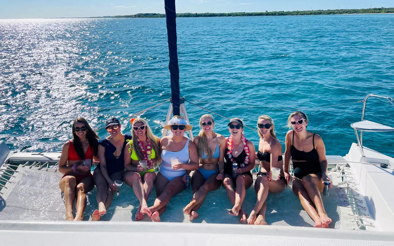 Row of women, several in flower leis, sitting on the catamaran's bow above sunlit Riviera Maya water