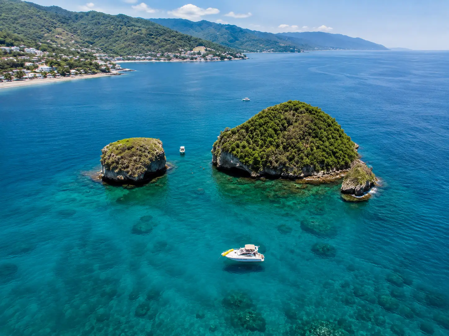 Aerial view of a motor yacht near two green rocky islets with the Puerto Vallarta coast beyond