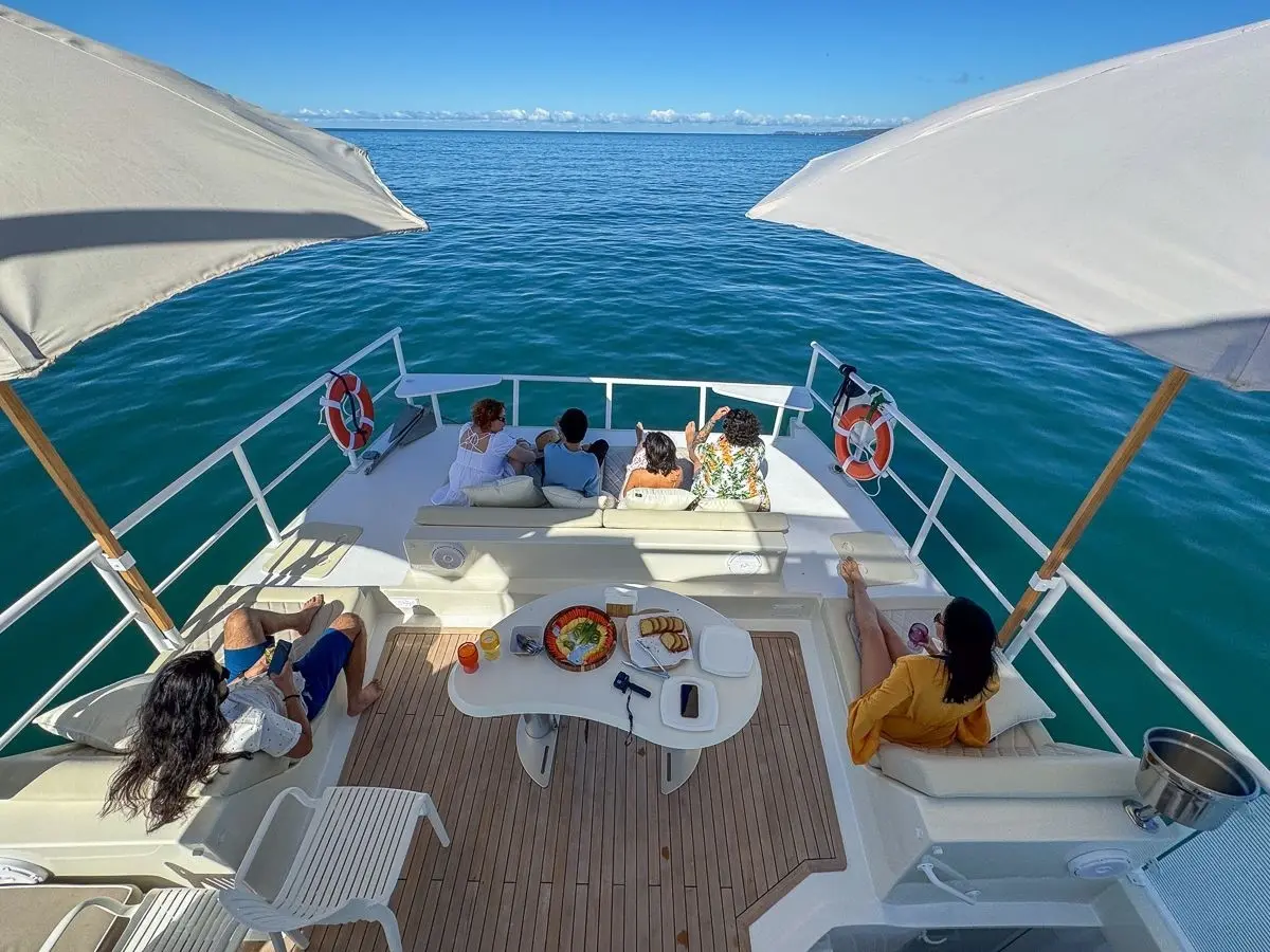 Guests relax around a snack table and bow seating under white parasols on the catamaran's deck