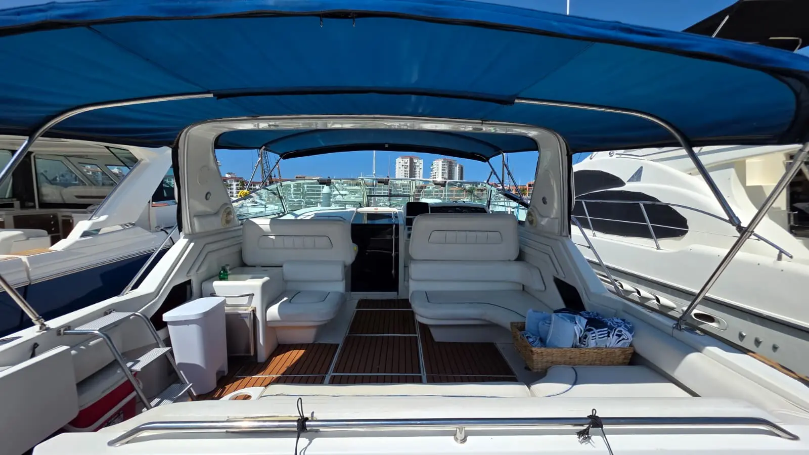 Open cockpit of the yacht under a blue bimini with twin seats facing the windshield and a teak floor
