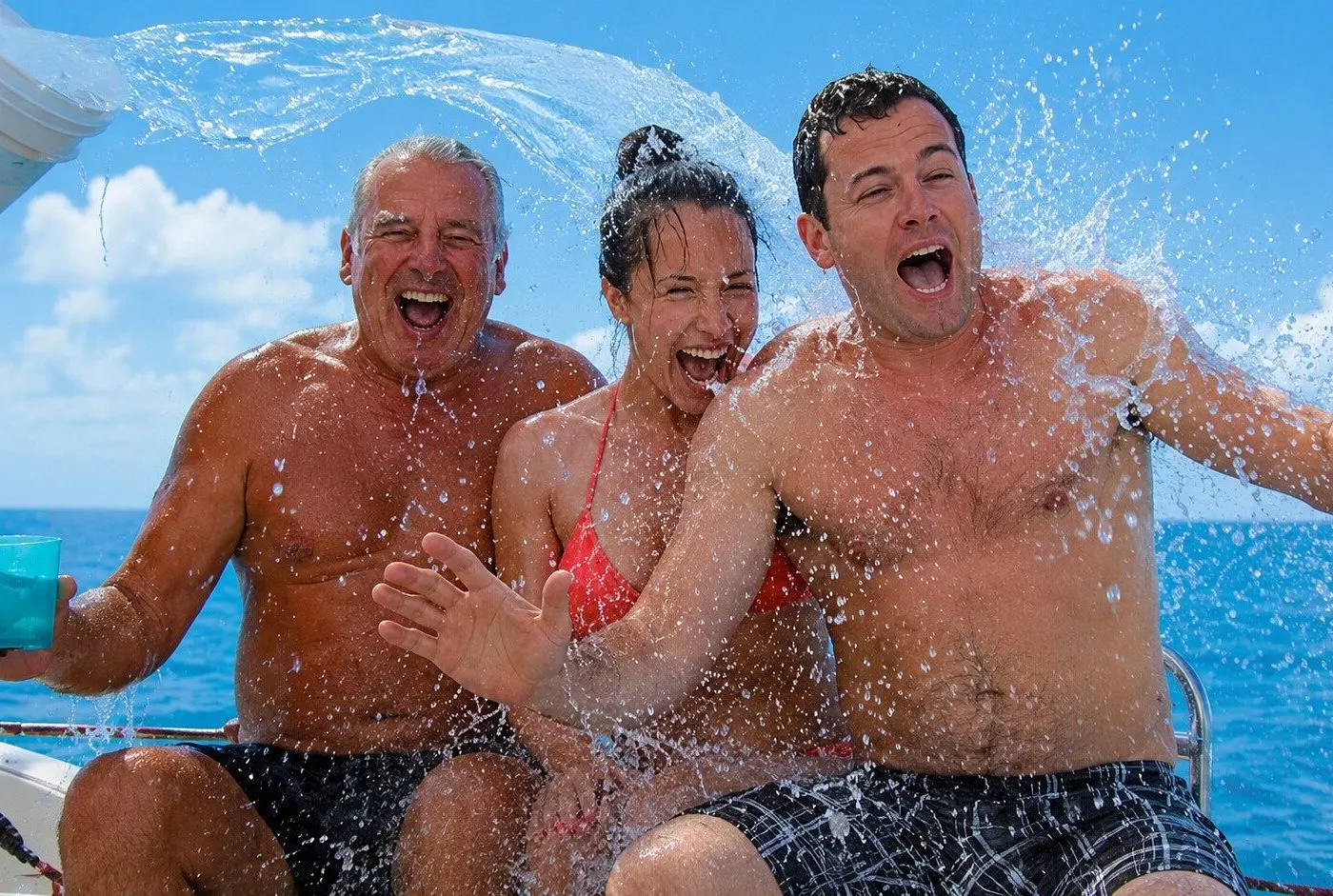 Three guests laughing as a splash of water drenches them on the catamaran deck