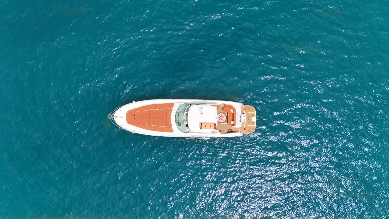 Top-down view of a white motor yacht with tan sun pads resting on teal water