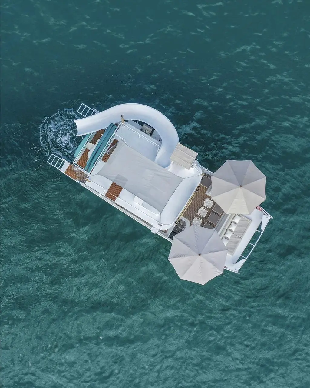 Top-down view of the party catamaran with its curving white water slide and parasols on green water
