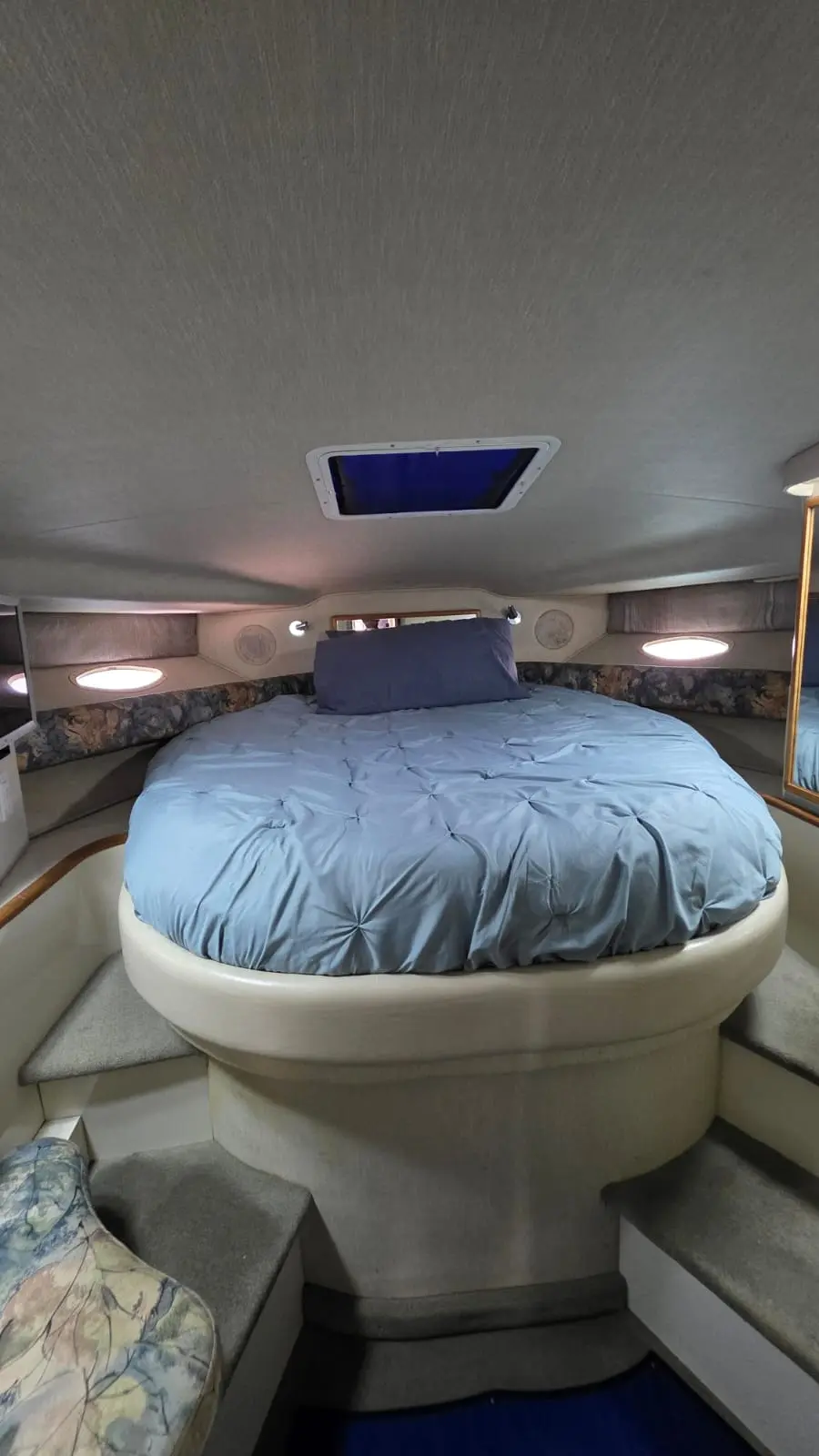 Forward cabin of the yacht with a blue-covered double bed beneath a skylight hatch