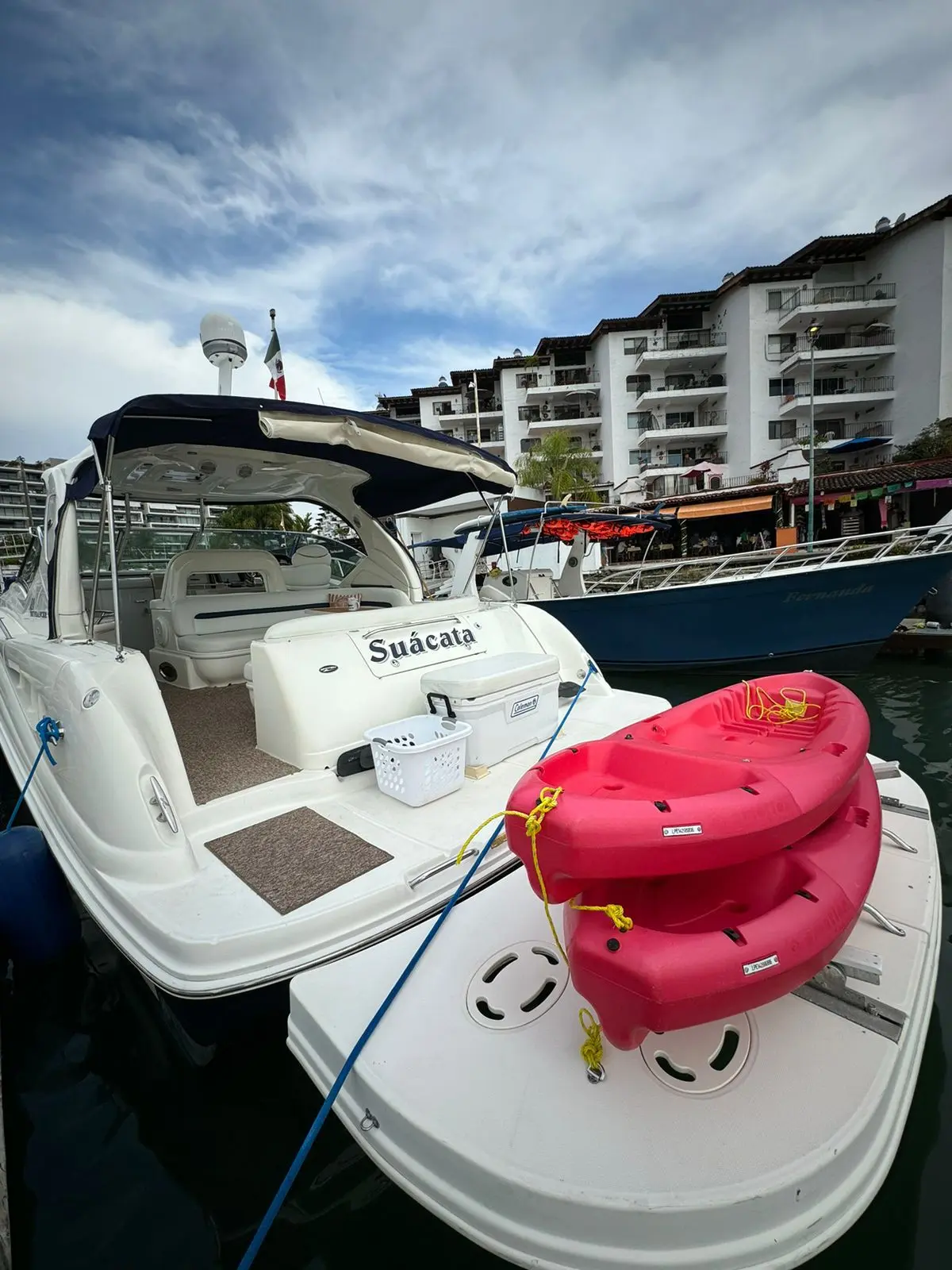 The motor yacht docked at a marina with red kayaks on its swim platform and waterfront buildings behind