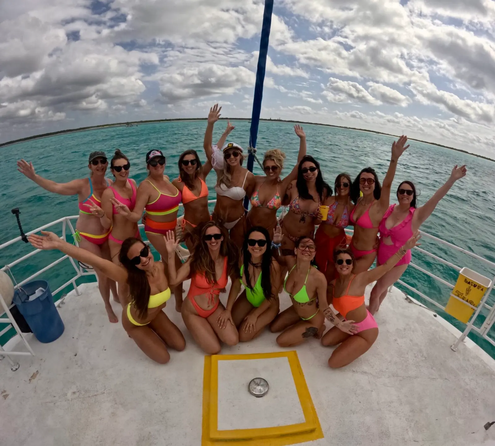 A large group of women in bright bikinis cheers on the catamaran's deck off Cozumel