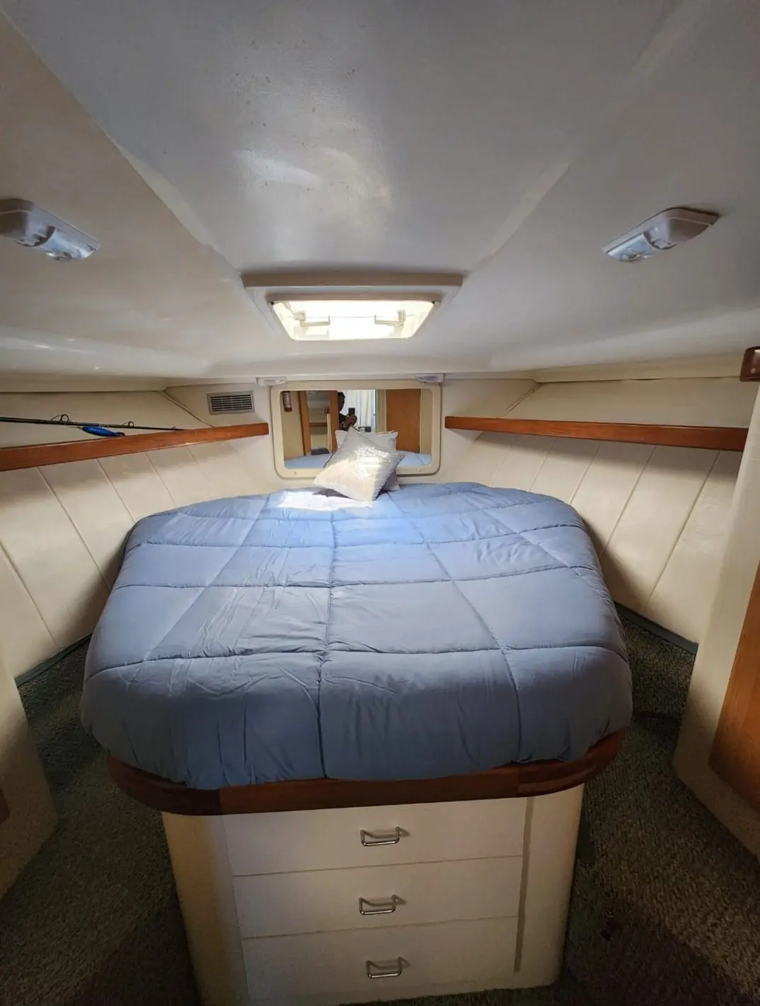 Yacht cabin with a blue-covered double bed above built-in drawers and an overhead hatch