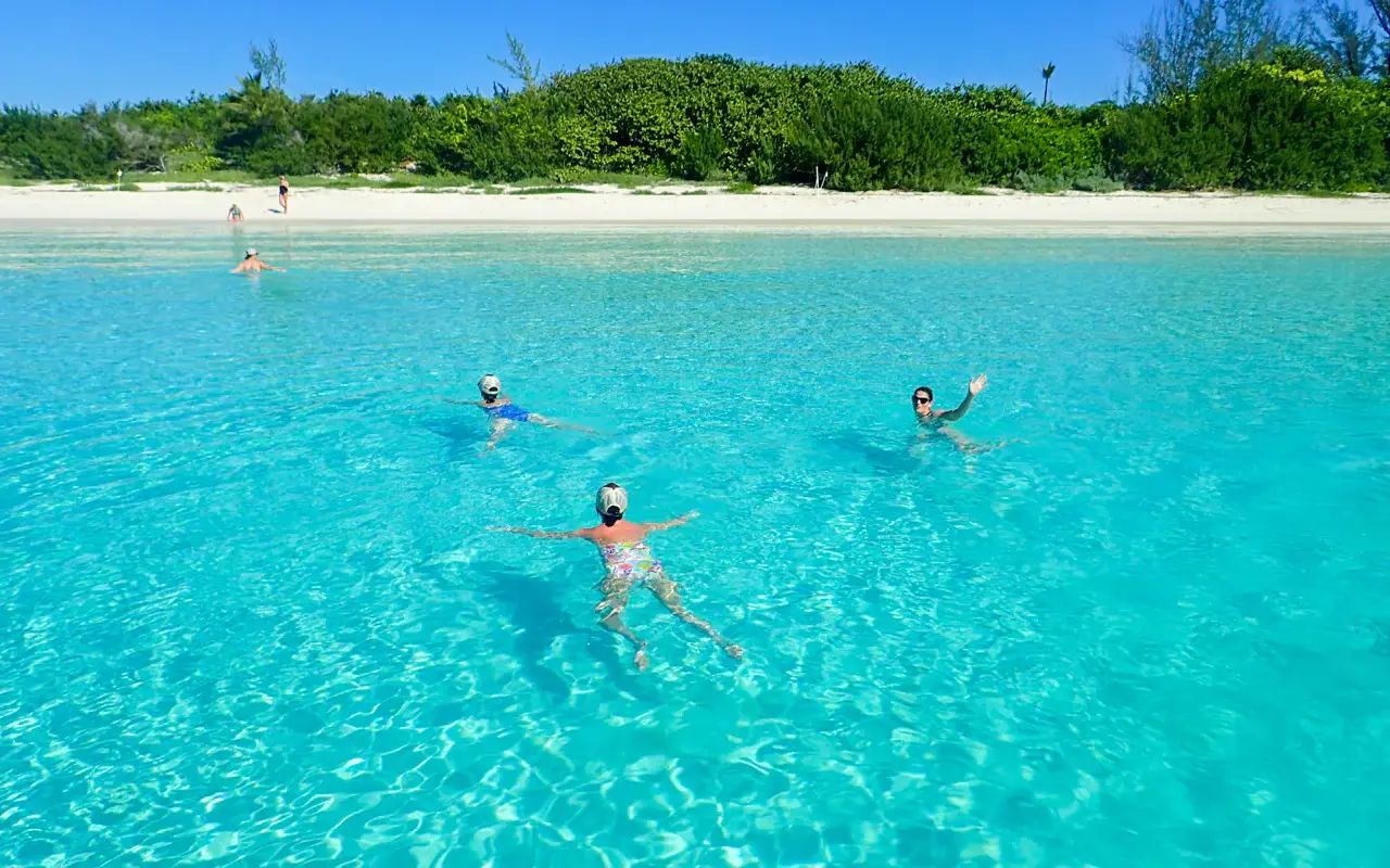 Guests swimming in clear turquoise water off a white-sand beach on the Riviera Maya