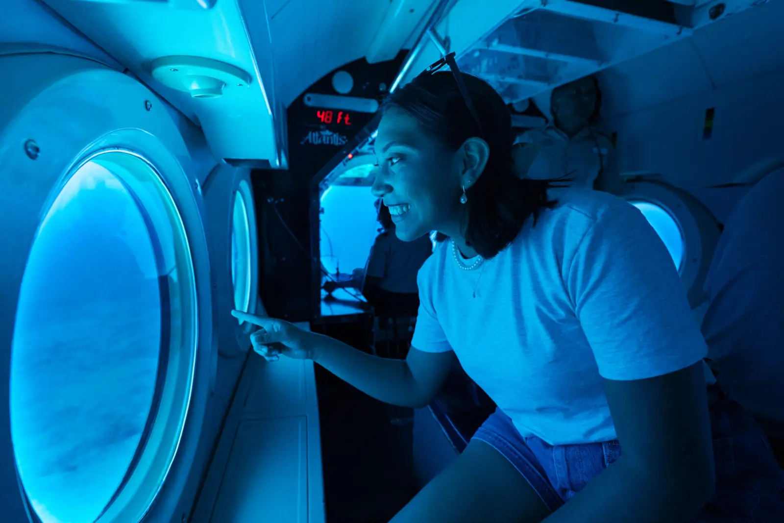 A smiling woman points out a porthole from her seat inside the submarine