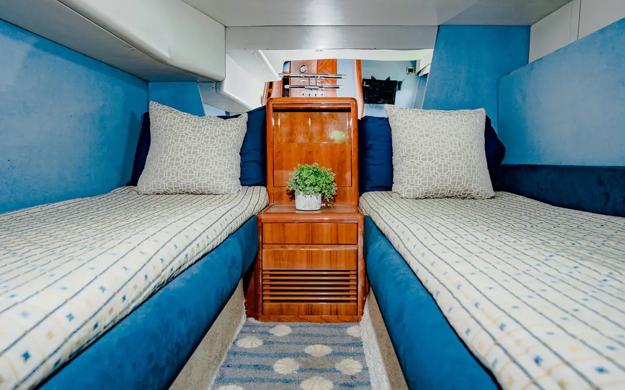 Twin guest cabin with two single beds in blue upholstery and a wooden nightstand