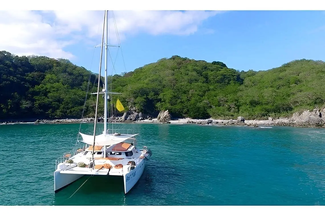 Sailing catamaran anchored in a calm turquoise cove below green hills on Banderas Bay