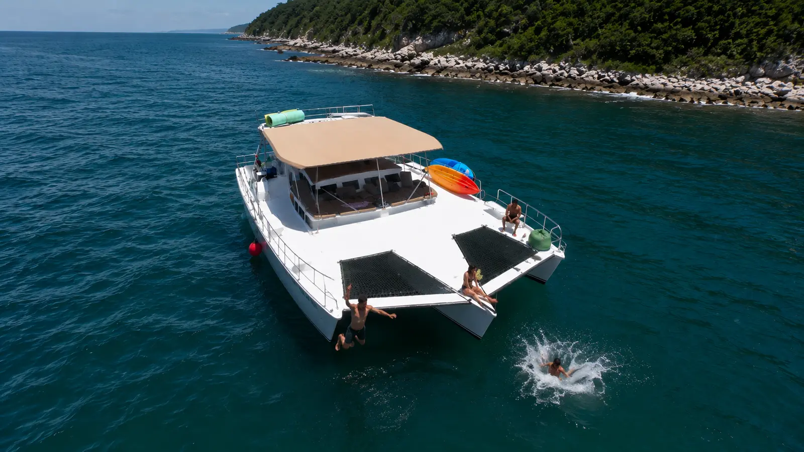 Aerial view of a trimaran anchored beside a rocky island near Puerto Vallarta as a guest splashes in