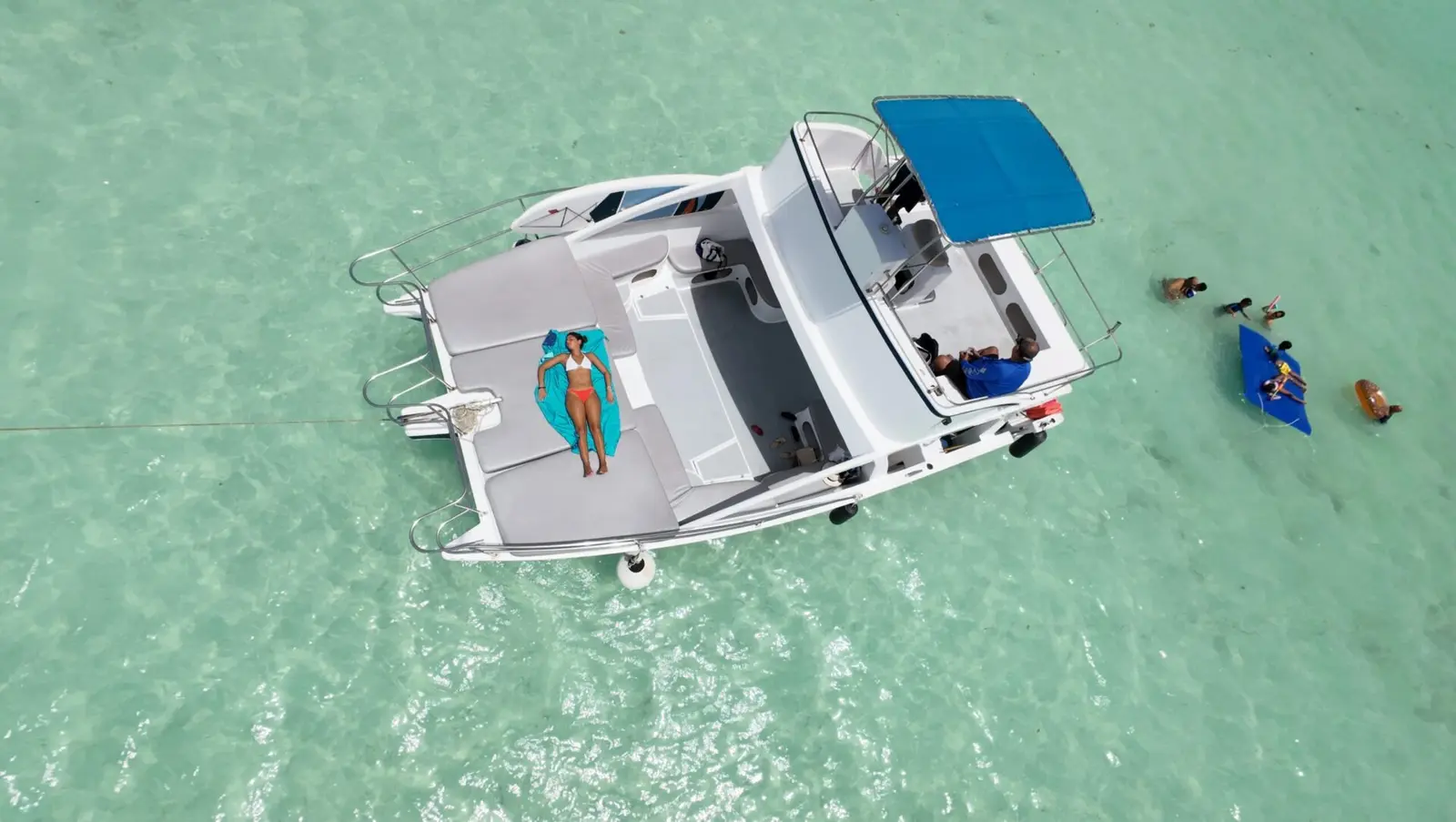 Overhead view of a woman sunbathing on the deck of a power catamaran as guests swim with a float nearby